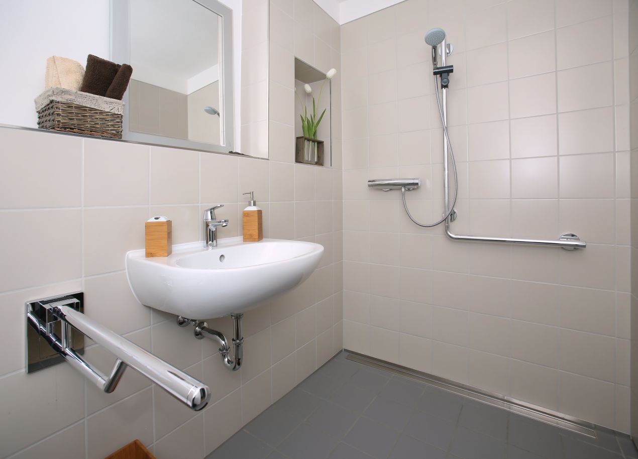 Rollstuhlgerechtes Bad mit Haltegriffen, bodengleicher Dusche und Designlösung als Teil eines Plattformlift-gerechten Umbaus